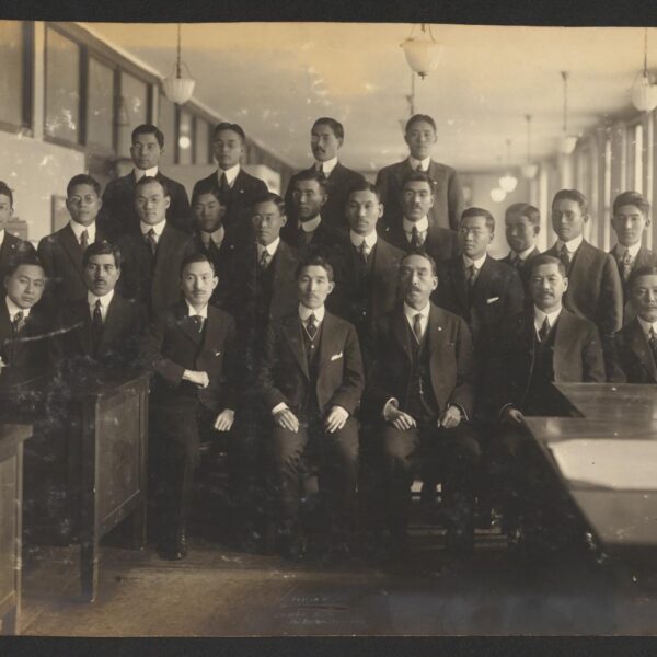 A black and white photograph showing a group of Japanese men in suits posing for a group photo inside a classroom.