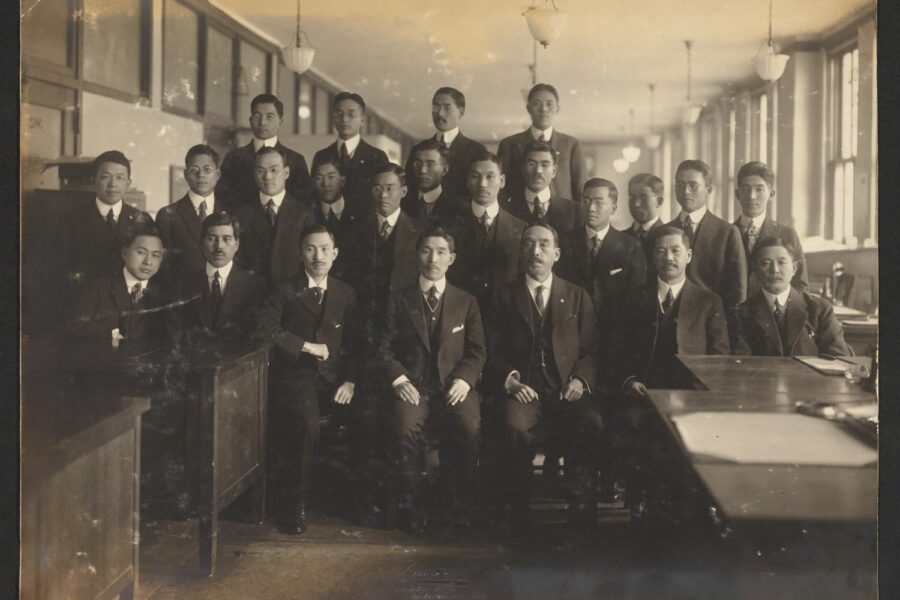 A black and white photograph showing a group of Japanese men in suits posing for a group photo inside a classroom.